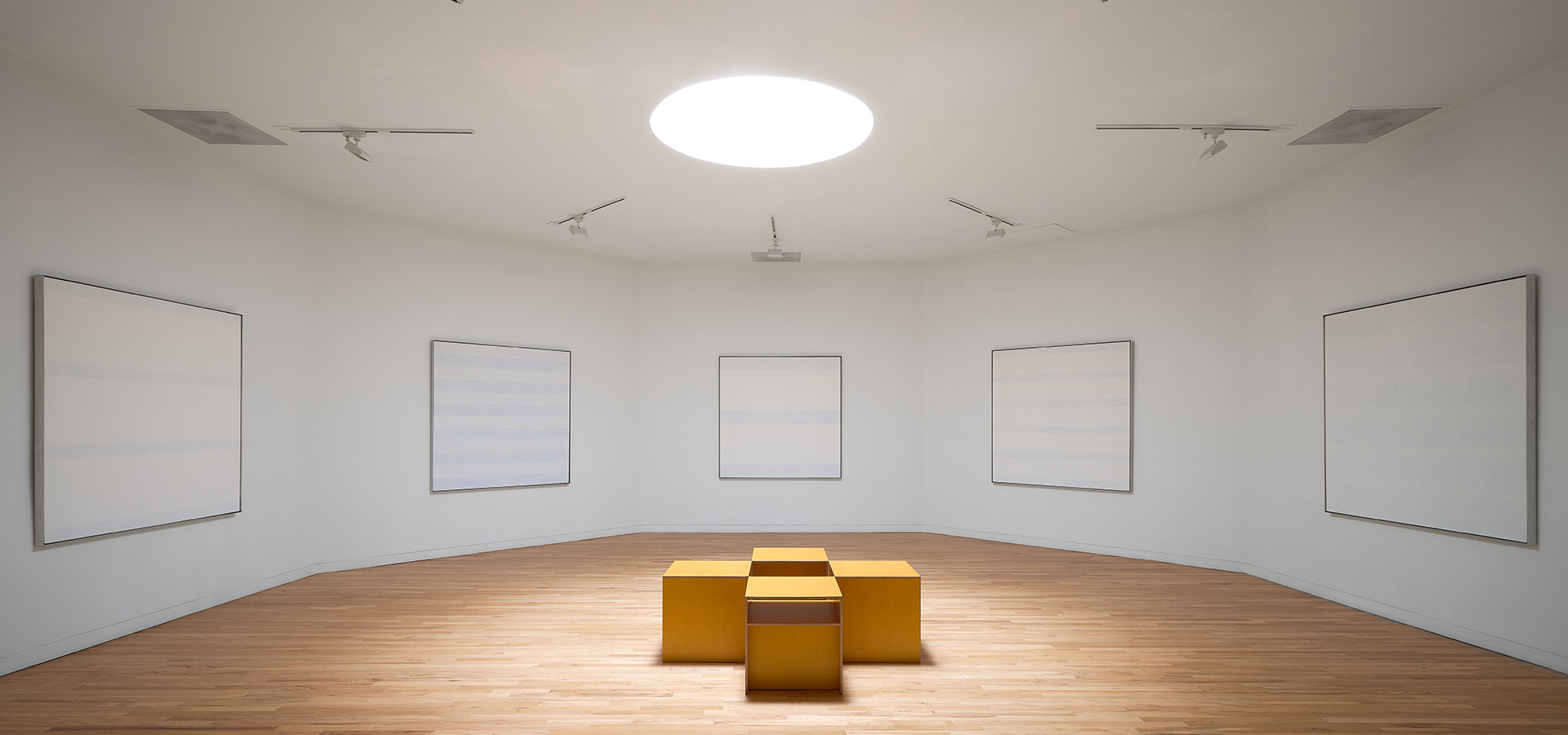 An octagonal shaped art gallery with multiple Agnes Martin paintings.