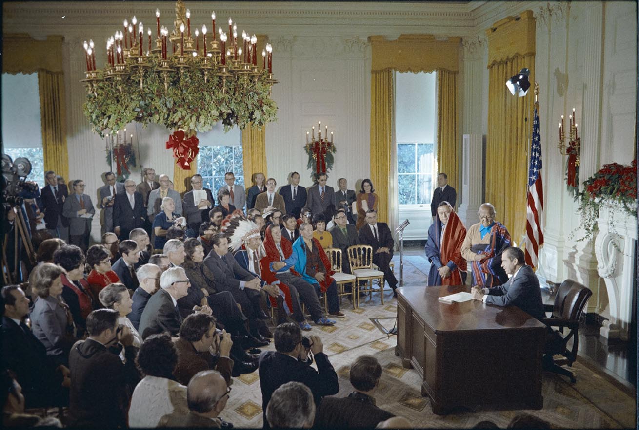 Archival Image of President Nixon in the Oval Office surrounded by a large crowd of supporters as he signs the bill to return Blue Lake to Taos Pueblo.