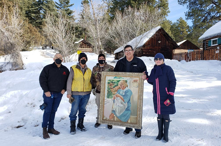Four people pose with a framed portrait outside of the D.H. Lawrence Ranch on a snowy day.