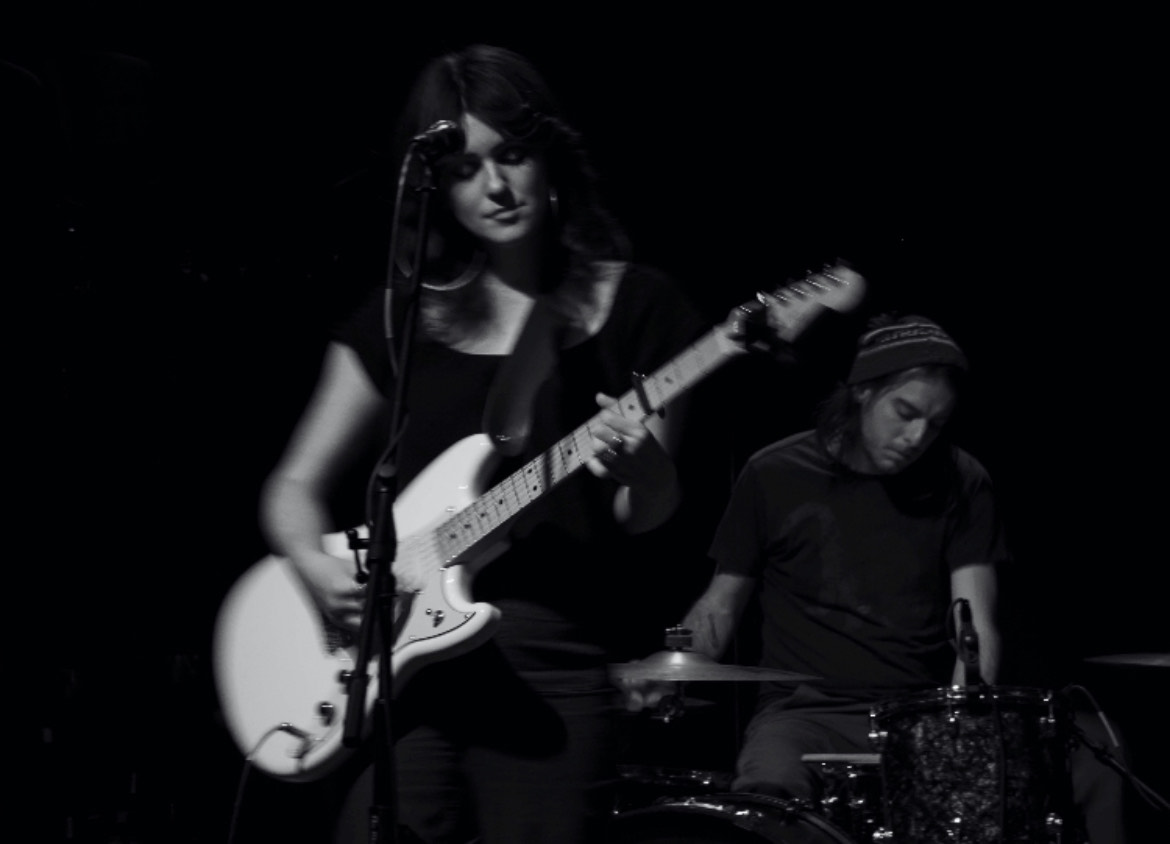 Black and white image of a rock band with female lead guitar and vocalist.
