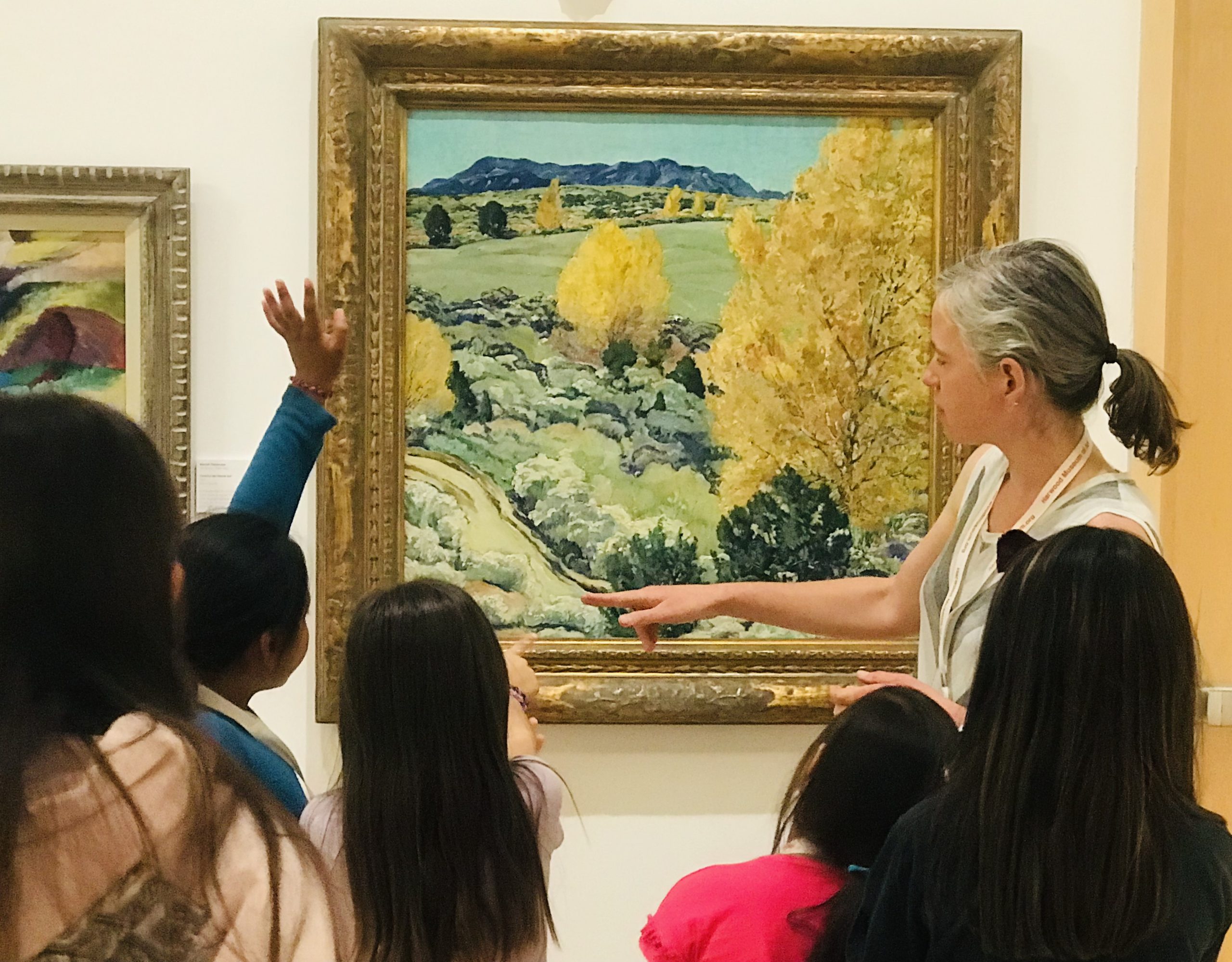 Children and an educator engage in conversation around a large landscape painting.  