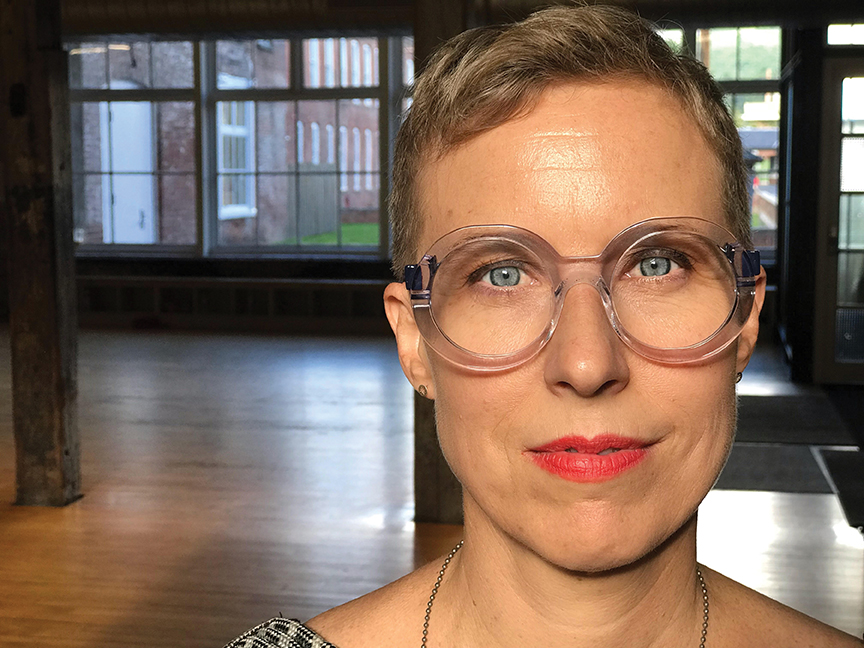 Headshot of Carrie Fonder, a light skinned woman with short hair, round chunky glasses, and red lipstick.