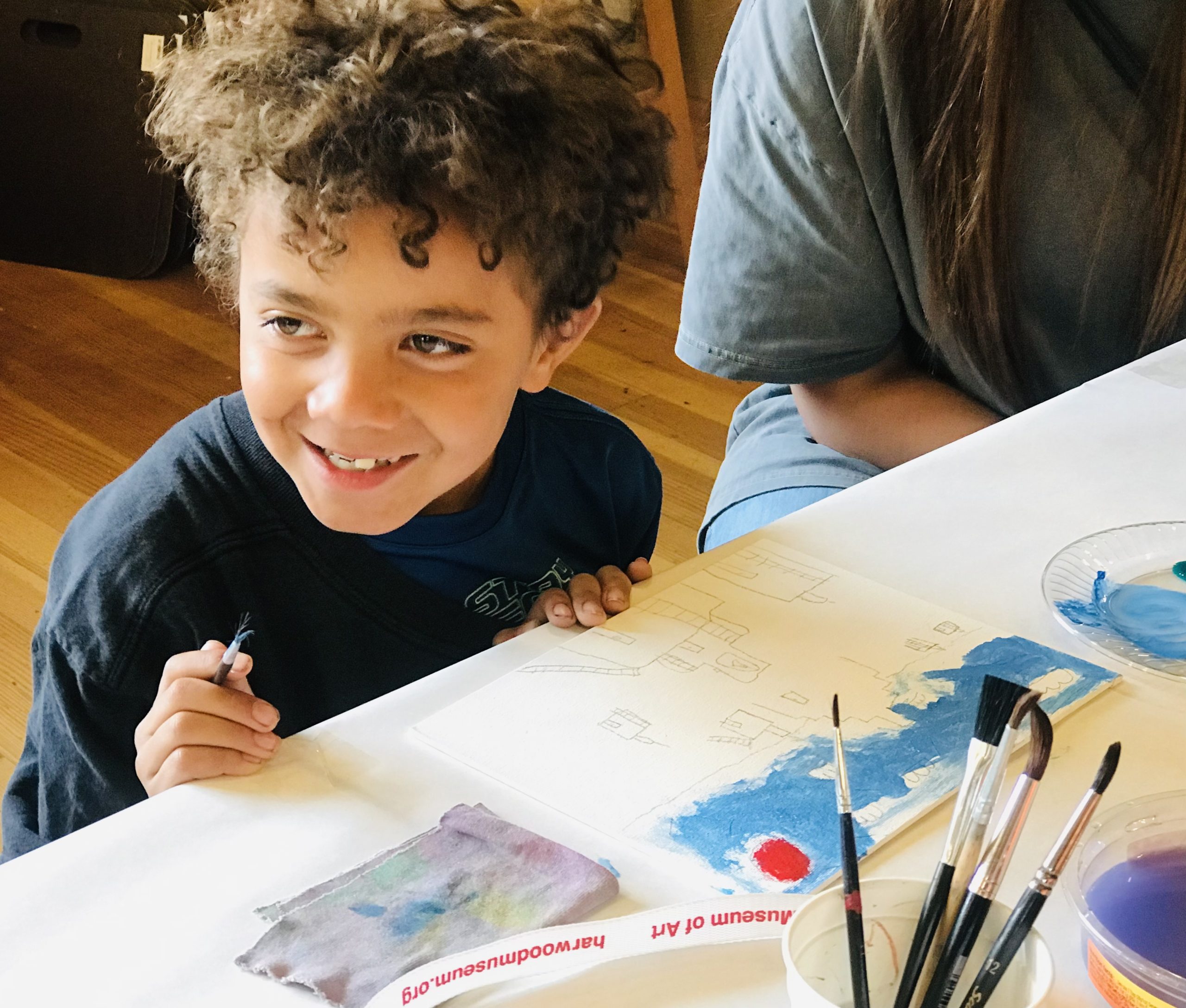 a young child smiles while in the middle of painting. 
