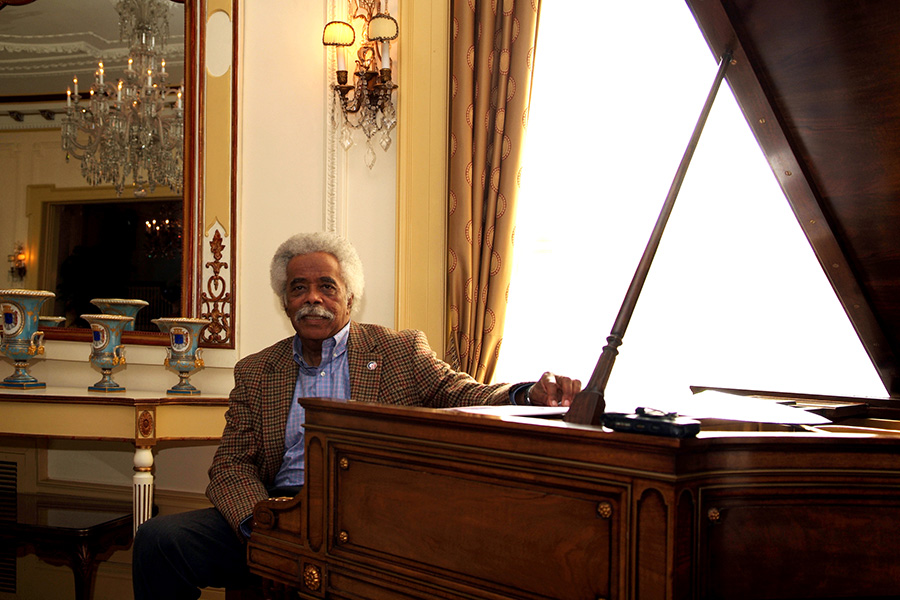 Purnell Steen, a Black man with short grey hair, sits at a piano in an elegantly furnished room.