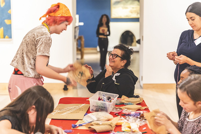 smiling patrons of various ages are making art around a table