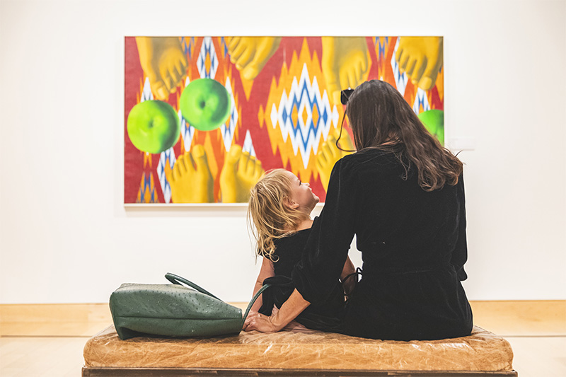 a seated mother and young daughter view artwork in the gallery