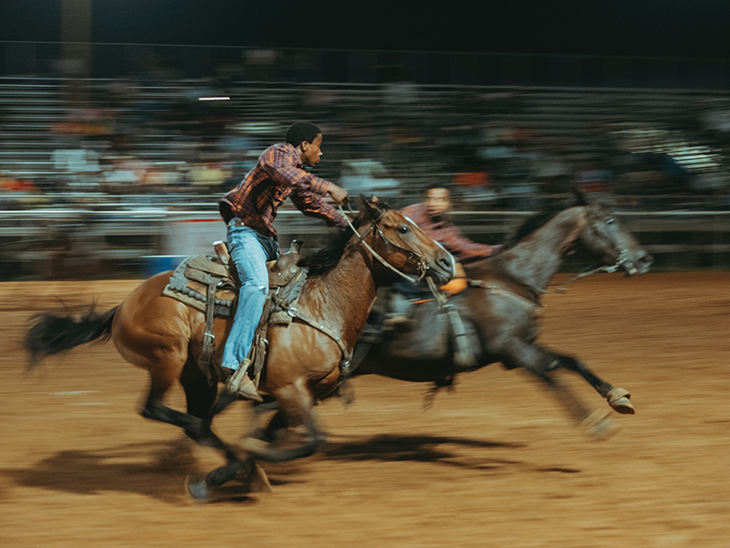 black cowboys ride horses running fast in a rodeo ring