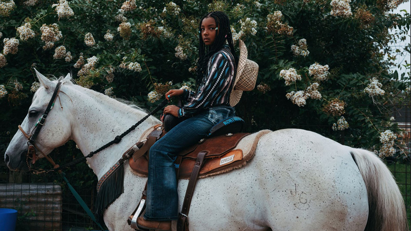 color photo of young black woman atop a white horse